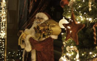 Ein Weihnachtsmann, Tannengrün, weiße Lichter und Kugeln sind als Weihnachtsschmuck im Schaufenster drapiert.
